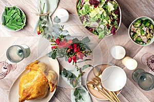 Festive family dinner table. Serving plates, bowls with salads and vegetables dishes, snack, whole roasted chicken, eucalyptus