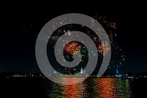 Festive fireworks in the dark sky with reflection in the water of the river at night