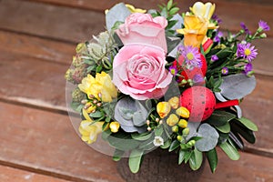 Festive flower arrangement of pink roses, yellow freesia flowers, eucalyptus leaves and other plants with red Easter eggs