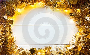 Festive frame made of gold garland with lights and tinsel on a white wooden background, copyspace. New year, Christmas, autumn and