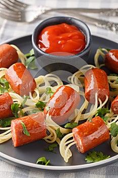 Festive funny food spaghetti with sausages and ketchup close-up in a plate. Vertical