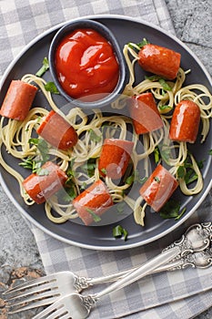 Festive funny food spaghetti with sausages and ketchup close-up in a plate. Vertical top view