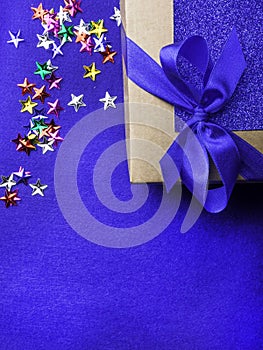 Festive gift wrapped present box with blue satin bow, decorated with colorful stars, close up isolated on trendy blue background