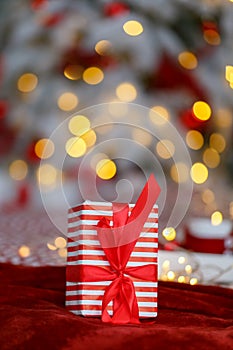 Festive gifts present with red ribbon under xmas tree lights and decoration abstract background. Christmas holiday concept.