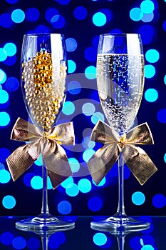Festive glasses with champagne, golden bows and beads on a glass table with a beautiful blue bokeh