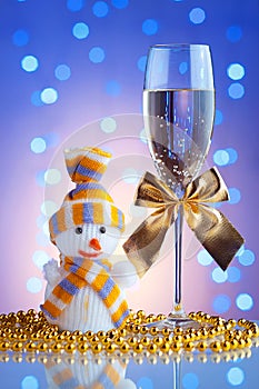 Festive glasses with champagne and golden bows, Snowman toy on a glass table with a beautiful blue bokeh