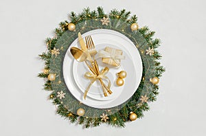 Festive golden table setting with a Christmas wreath and New Year decorations on a gray background. Copy space, top view, flat lay