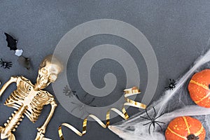 Festive halloween composition with white cobweb, spiders, pumpkins, bats and golden skeleton over gray concrete background