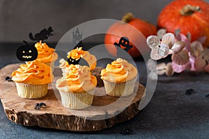 Festive Halloween cupcakes with scary toppings on vintage wooden board on dark background. Pumpkin cupcakes with black decorations
