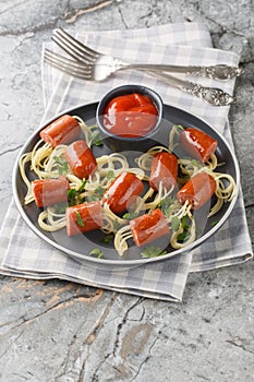 Festive idea of spaghetti with sausages and ketchup close-up in a plate. Vertical