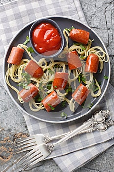 Festive idea of spaghetti with sausages and ketchup close-up in a plate. Vertical top view