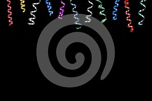Horizontal image with multi coloured rolls curly ribons hanging from the top on black bacgroung photo