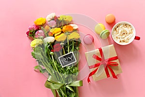 Festive morning concept buttercup flowers bouquet, gift box, cup of cappuccino and makarons cake on the pink background.