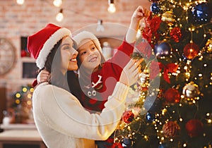 Festive mother and daughter decorating Christmas tree at home