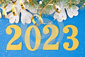 Festive New Year background with golden numbers 2023, sparkles, snowflakes, decorations and Christmas tree branches on blue