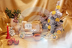 Festive party atmosphere with modern Halloween tree. Cozy Halloween decorations with candles, orange mug, dry flowers