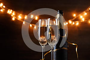 Festive photo of two wine glasses with wine, bottles, cork, burning garland