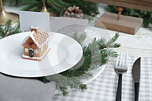 Festive place setting with beautiful dishware, cutlery and gingerbread house card holder for Christmas dinner on white wooden