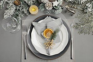Festive place setting with beautiful dishware, fabric napkin and dried orange slice for Christmas dinner on grey table, flat lay