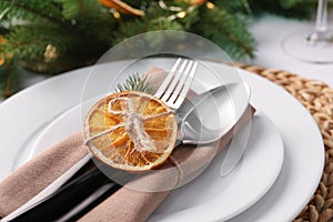 Festive place setting with beautiful dishware, fabric napkin and dried orange slice for Christmas dinner on white table, closeup