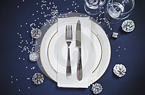 Festive place setting for Christmas holiday dinner. Beautiful cutlery on the white napkin and two white plates. Wineglasses,