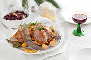 Festive poultry dinner, roast chicken with fruits and herbs, served with red cabbage and wine on a white table pine branches,
