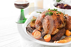 Festive poultry meal, roast chicken with kumquat, spices and herbs on a white table with red cabbage and wine, holiday dinner for