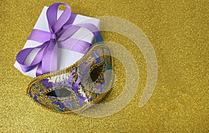 Festive purple carnival mask, gift box on glitter golden background.