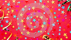 Festive red background with multicolor star confetti and streamers. Background for birthdays, christmas, anniversary