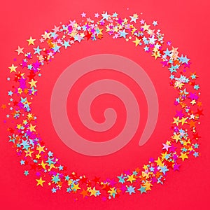 Festive red background with multicolor star shape confetti, copy space. Background for birthdays, christmas, anniversary