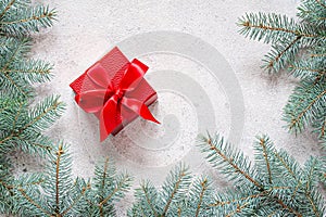 Festive red gift box decorated with a satin ribbon and fir branches on a gray background.