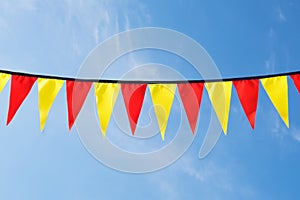 Festive ribbon of red and yellow triangle flags on the white clouds and blue sky background