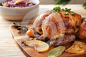 Festive roast chicken fresh from the oven with apples, kumquat, spices and herbs served with red cabbage on a wooden table,