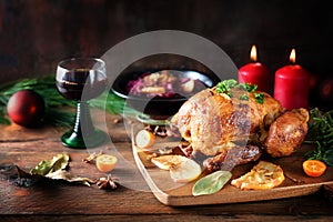 Festive roast chicken with red cabbage, citrus fruits, herbs and wine on a dark rustic wooden board with candles and Christmas