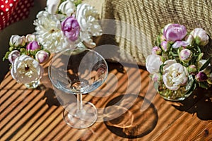 Festive rustic still life with glass empty clear glass surrounded by white flowers on textile background on wooden table. Diagonal
