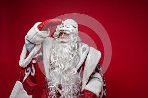 Festive Santa Claus look into the distance with hand on forehead on red background, copy space for holiday advertising