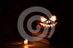 Festive scary halloween pumpkin on a stack of old books with candles