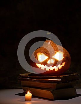 Festive scary halloween pumpkin on a stack of old books with candles