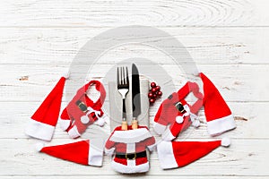 Festive set of fork and knife on wooden background. Top view of new year decorations and santa clothes and hat. Christmas concept