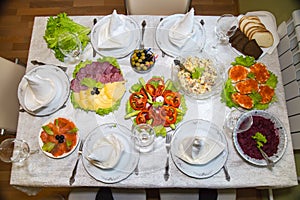 Festive set table with plates of salads, appetizer of vegetables and fruits, sliced sausage cheese, top view. Holiday, food