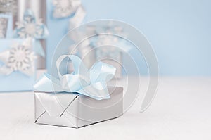 Festive silver metallic gift box with blue silk bow closeup and different elegance soft christmas presents on background in blur.