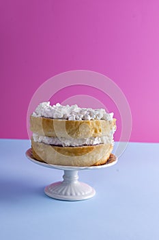 A festive sponge cake with white cream for a birthday, on a pink and blue background. Food for the holiday. Advertising poster and