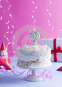 A festive sponge cake with white cream for a birthday, on a pink and blue background. Tinsel, waverki and boxes of gifts. Question