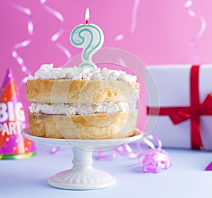 A festive sponge cake with white cream for a birthday, on a pink and blue background. Tinsel, waverki and boxes of gifts. Question