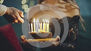 Festive sweet cake with candle which lighting on lighter, burner or fire. Close up of hands holding cake on plate