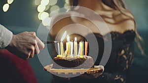 Festive sweet cake with candle which lighting on lighter, burner or fire. Close up of hands holding cake on plate