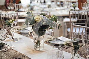 Festive table arrangement. White and blue flower bouquet in transparent glass vase. Celebration, wedding, birthday