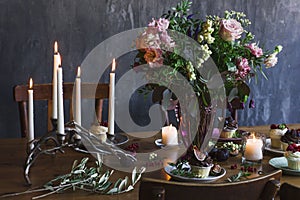 Festive table with bouquet of flowers, candles and cupcakes