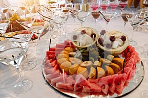 Festive table with cold exotic alcoholic beverages, cocktails, watermelon, grape, banana and different fresh fruits.