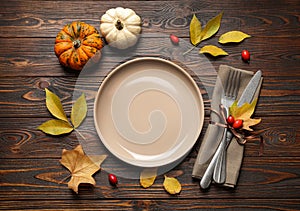 Festive table setting with autumn leaves and pumpkins on wooden background, flat lay. Thanksgiving Day celebration